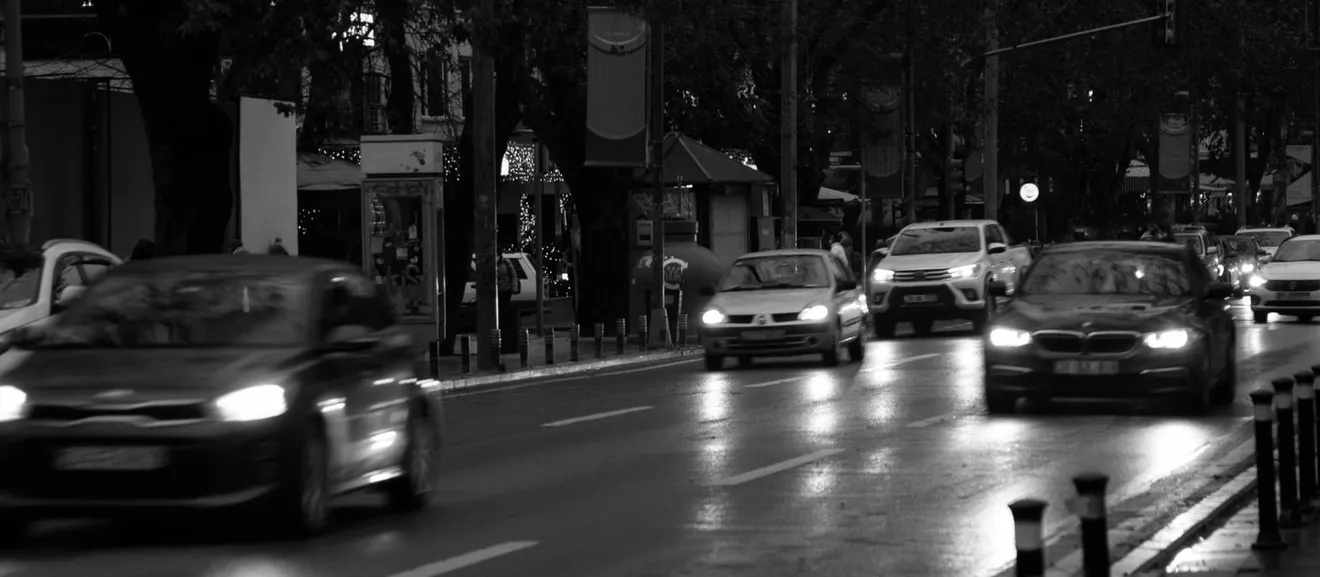 Ασπρόμαυρη εικόνα κίνησης τη νύχτα, με αυτοκίνητα με αναμμένα φώτα κάτω από φωτισμό δρόμου.