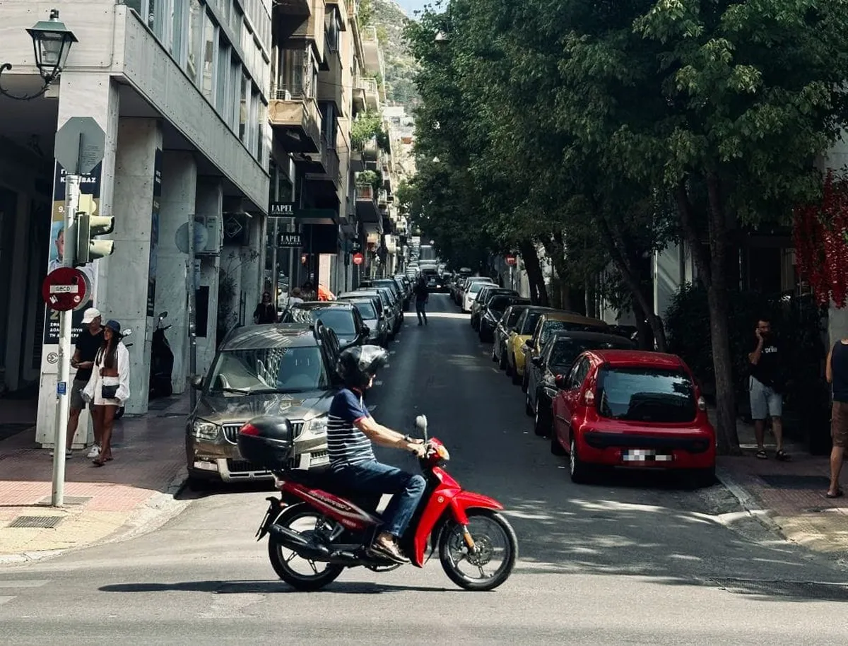 δρόμος πόλης μέρας για το θέμα πινακίδες κυκλοφορίας. Παρκαρισμένα αυτοκίνητα, μηχανάκι και πεζοί σε κίνηση σε ανηφορικό δρόμο.