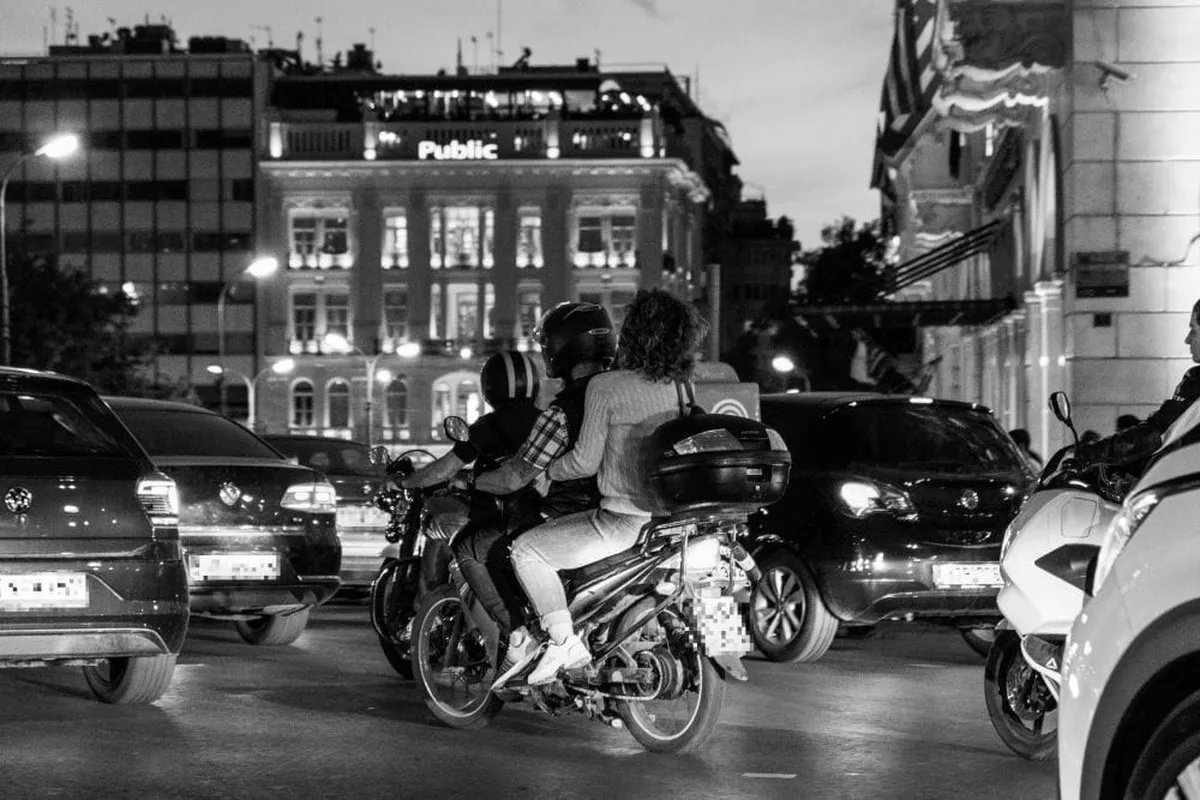 ασπρόμαυρη εικόνα, νύχτα, μεγάλος δρόμος μέσα σε πόλη με αυτοκίνητα και μηχανές εν κινήσει, στο βάθος κτήρια
