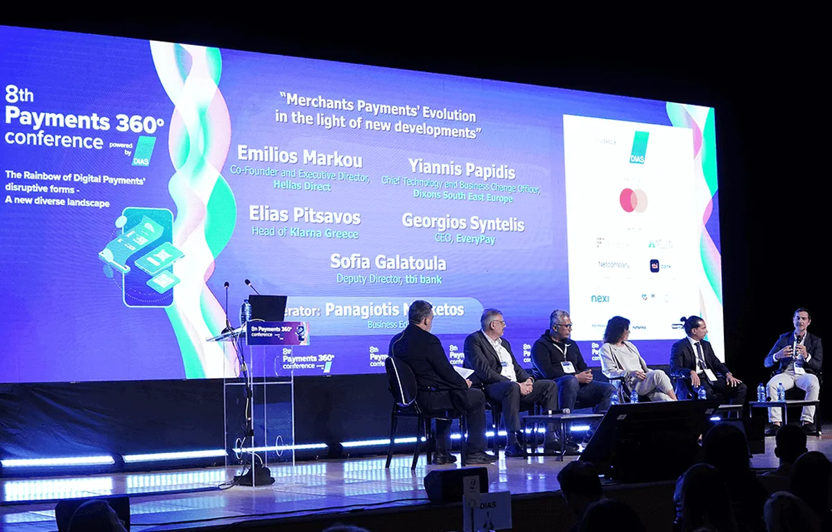 πάνελ έξι ανθρώπων καθιστών σε σκηνή, podium στα αριστερά, στην οθόνη παρουσίαση με τα ονόματα των ομιλητών